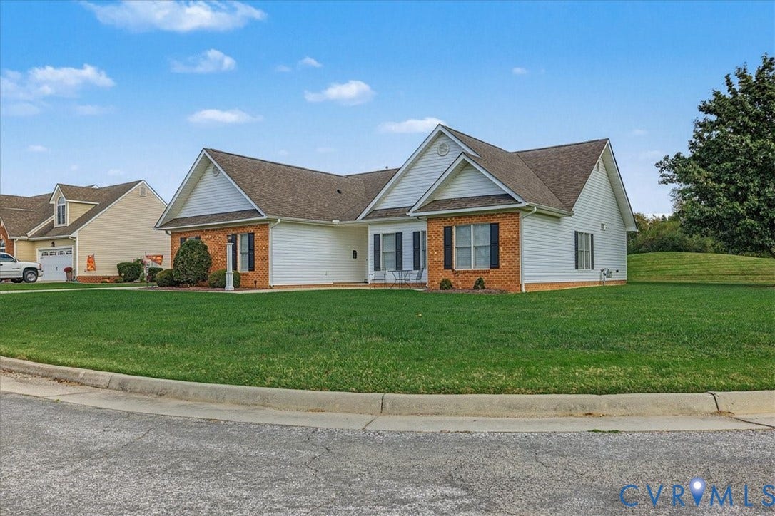 Exterior featuring a brick and vinyl siding facade, multi-gabled roofline, and shuttered windows, situated on a corner lot with an open lawn