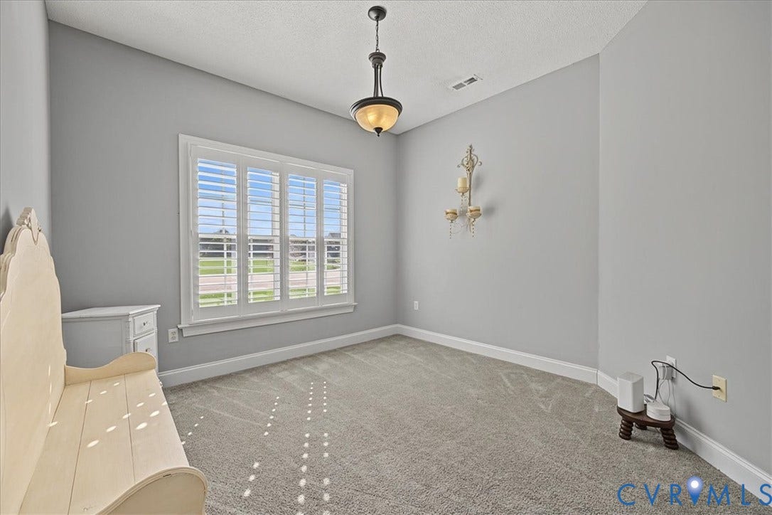 Interior room featuring wall-to-wall carpeting, large multi-pane window with interior shutters, tiered light fixture with frosted glass, and a decorative wall-mounted metal sconce