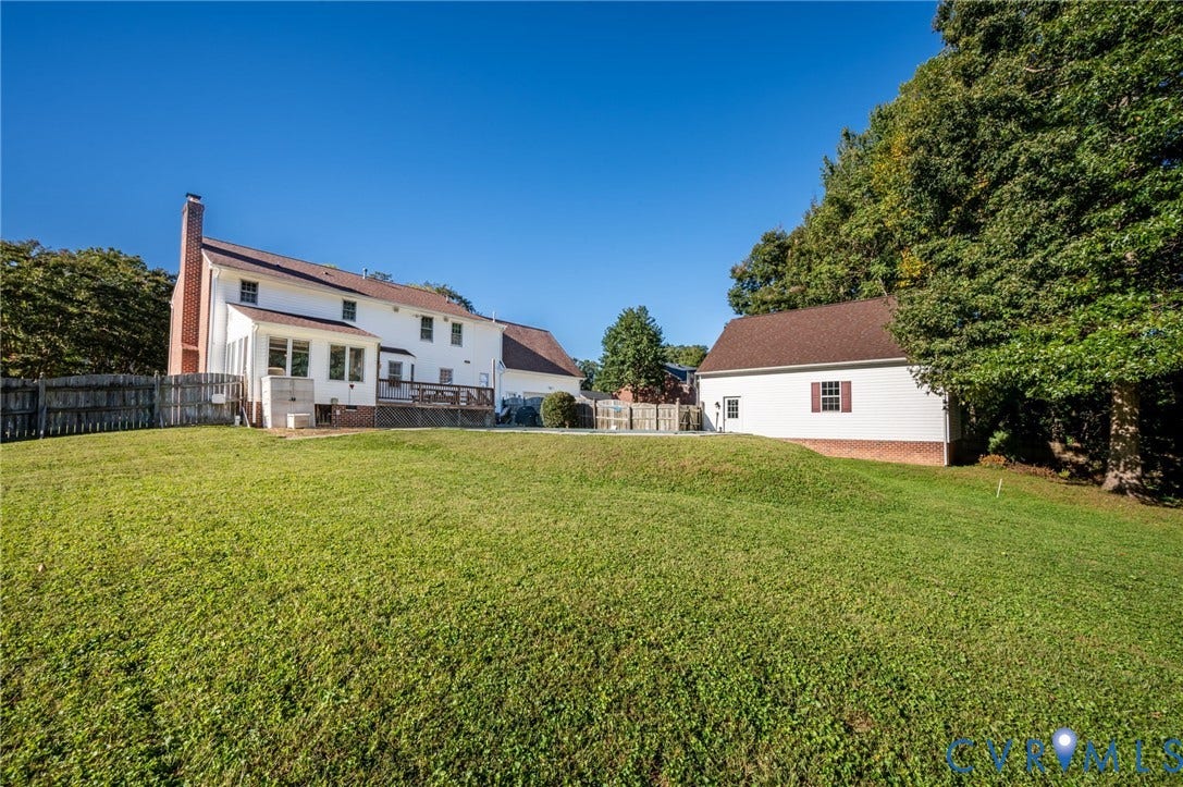 Expansive green lawn with a two-story white exterior home, a brick chimney, and a composite decked patio