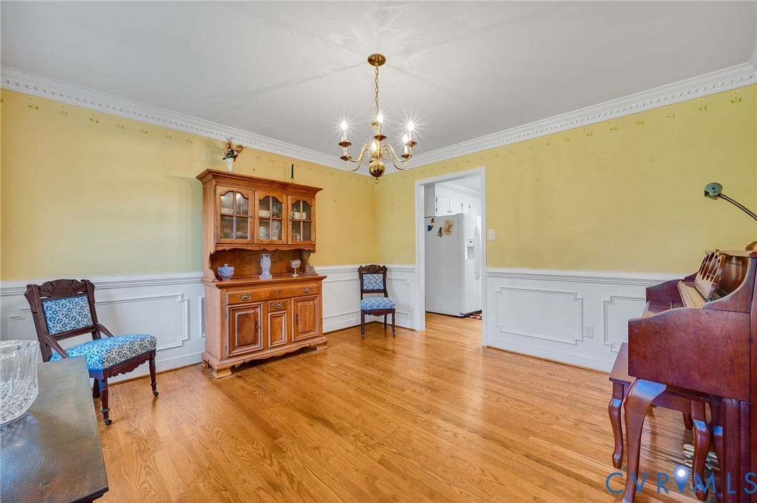 Hardwood flooring, crown molding, chair rail with decorative wainscoting, and an overhead chandelier