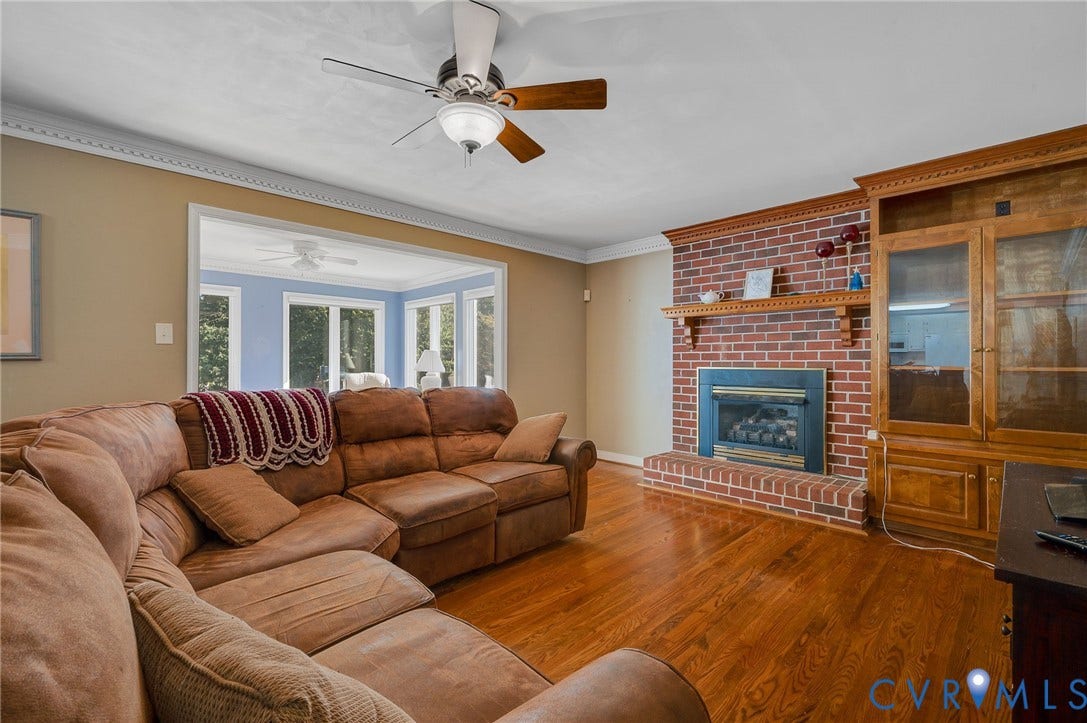 Hardwood flooring, brick-faced fireplace with hearth, wood mantel, built-in wood cabinetry, and crown molding