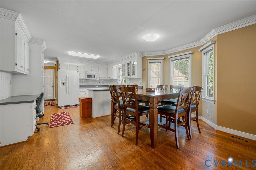 Open-concept kitchen and dining area featuring wood-finish flooring, white cabinetry, integrated appliances, and a bay window