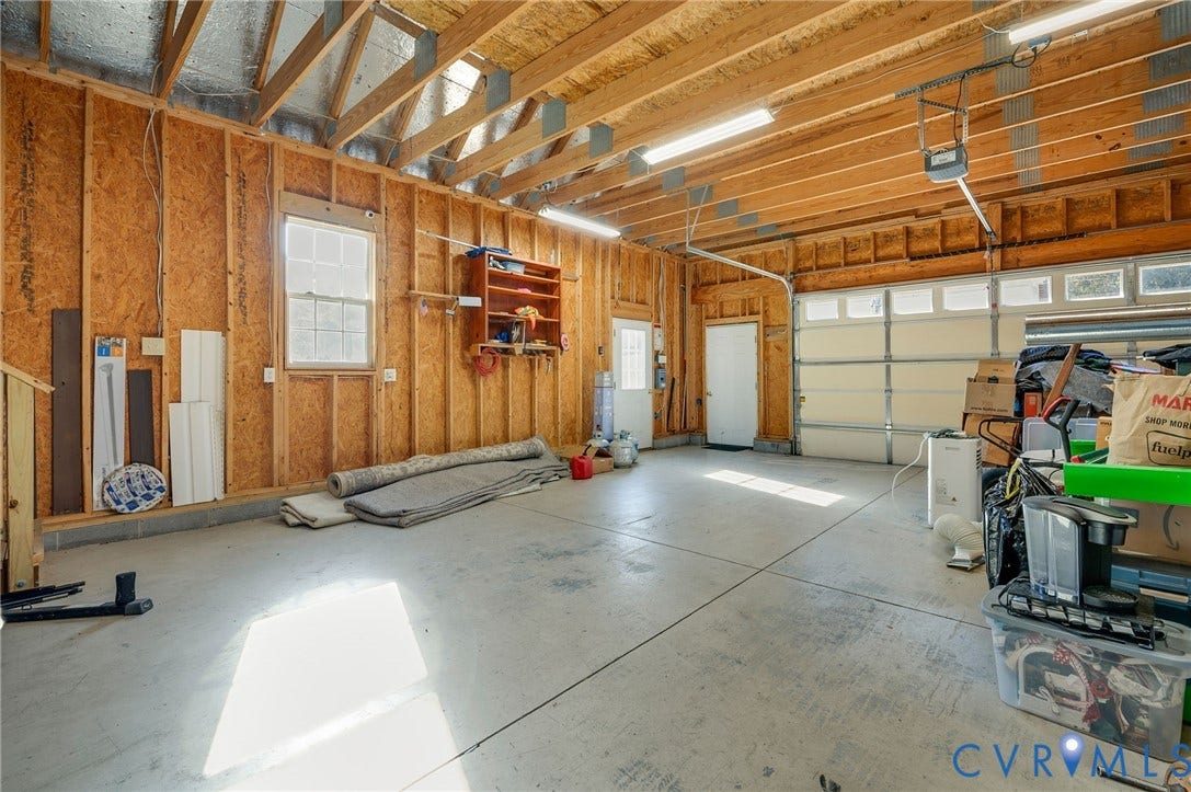 Spacious garage with exposed wood rafters, concrete flooring, and multiple windows