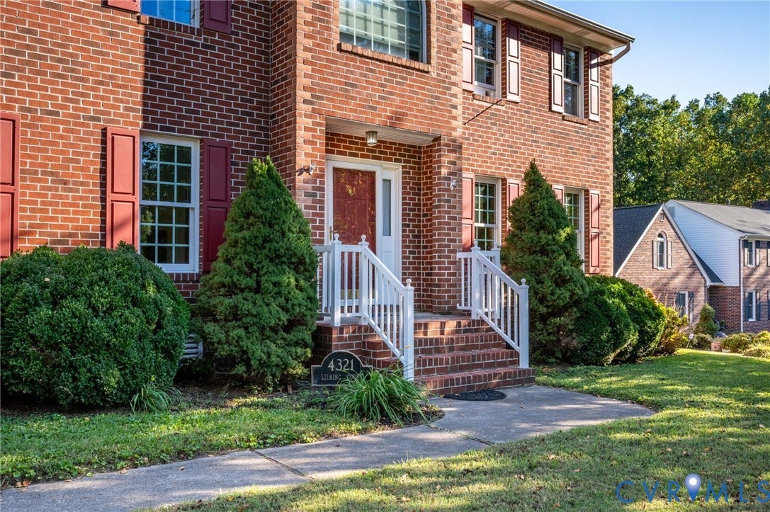 Brick exterior with red shutters, white trim windows, brick steps, and white railings