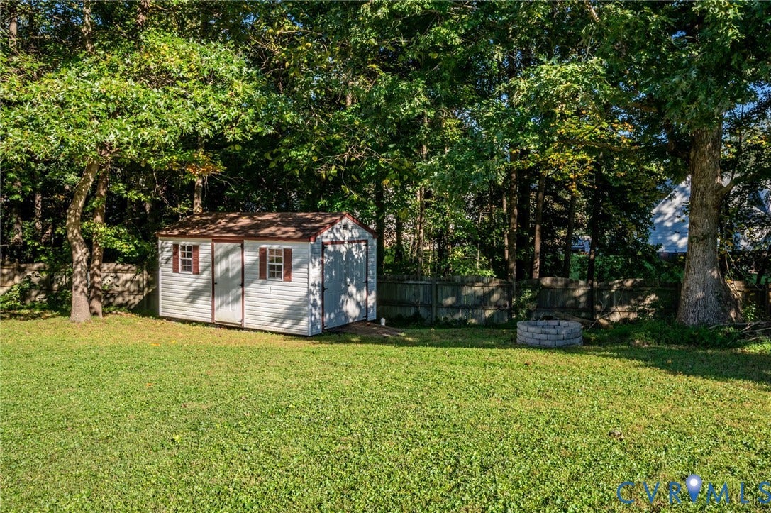 Expansive backyard featuring a lush lawn, white siding shed with brown trim, mature trees, and a stone-ringed fire pit