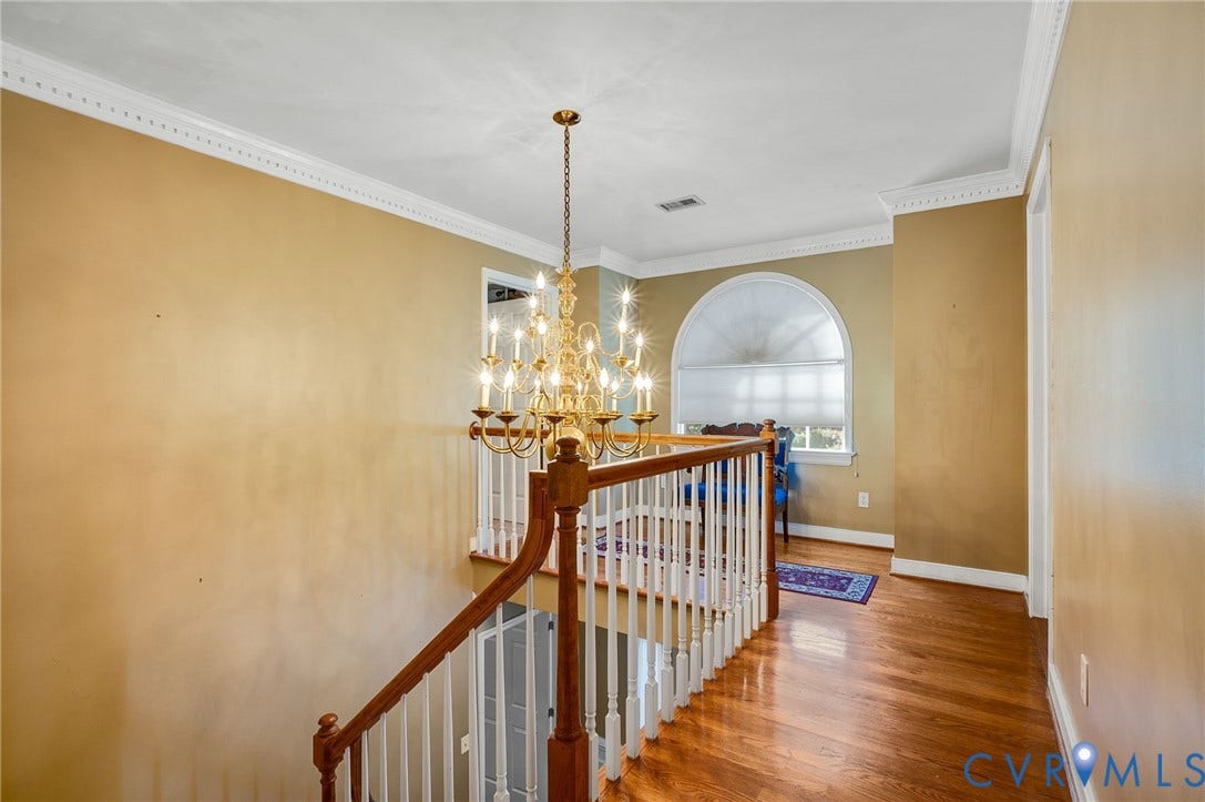 Hardwood flooring, ornate chandelier, arched window, white crown molding, and white spindle railing