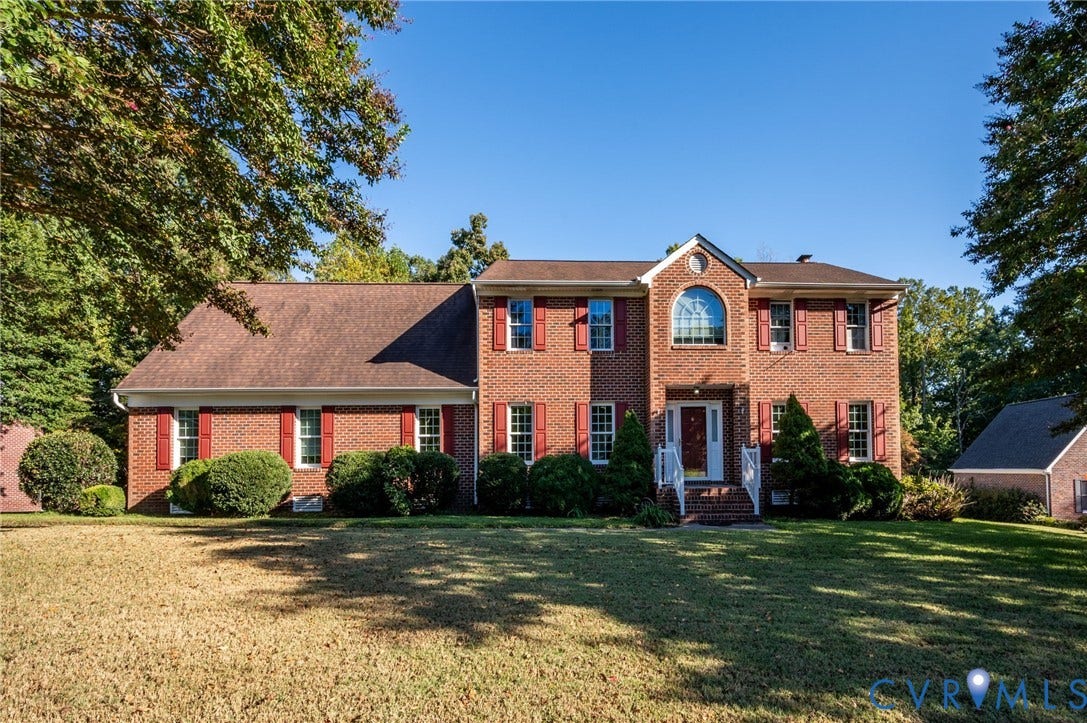 Brick exterior, arched window, red shutters, front porch with white railing, mature landscaping