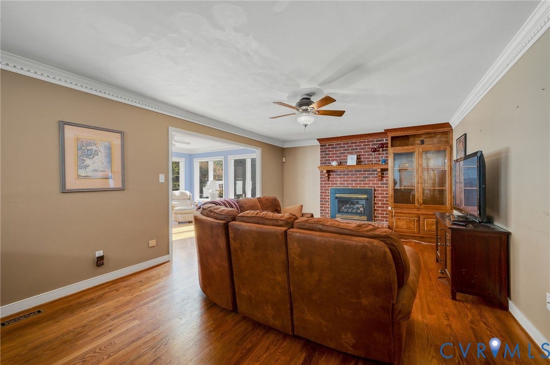 Hardwood flooring, crown molding, a brick-surround fireplace with a wooden mantel, and a built-in wooden cabinet