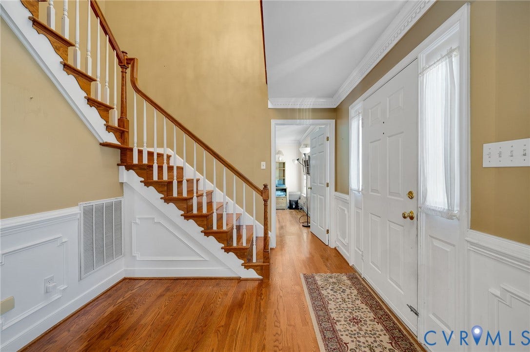 Hardwood flooring, painted wainscoting, crown molding, white paneled doors, and a hardwood staircase with wood risers