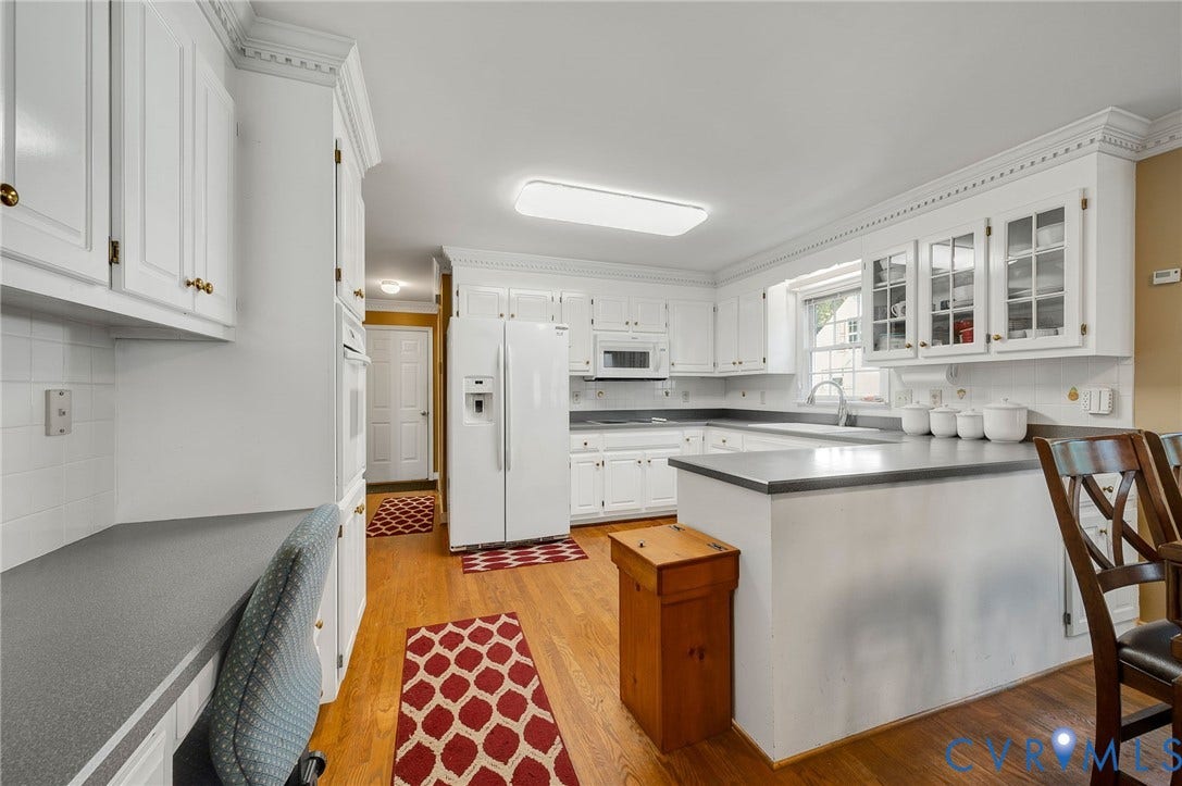 Kitchen featuring white cabinetry, gray countertops, wood-finish flooring, and a built-in desk area