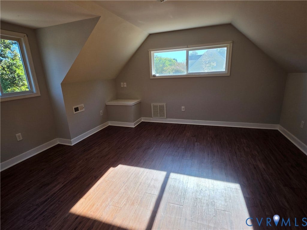 Wood-finish flooring with crisp white baseboards, multiple windows, and a built-in storage bench