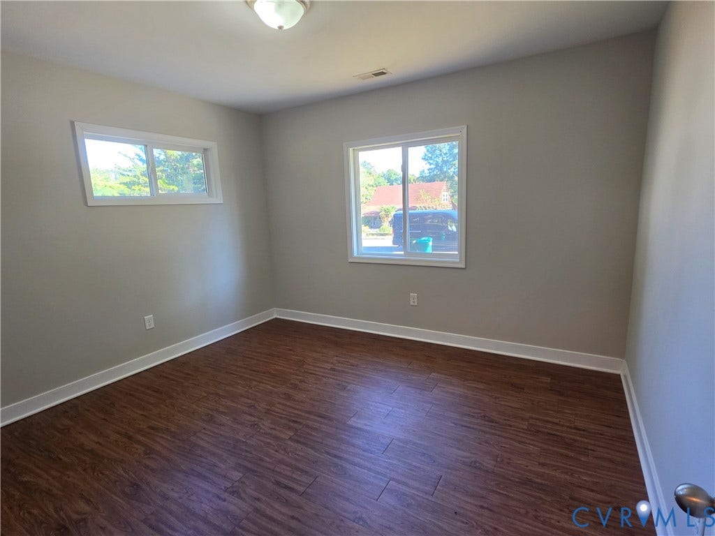 Wood-finish flooring, neutral wall tones, white trim, two windows, and a flush mount ceiling light