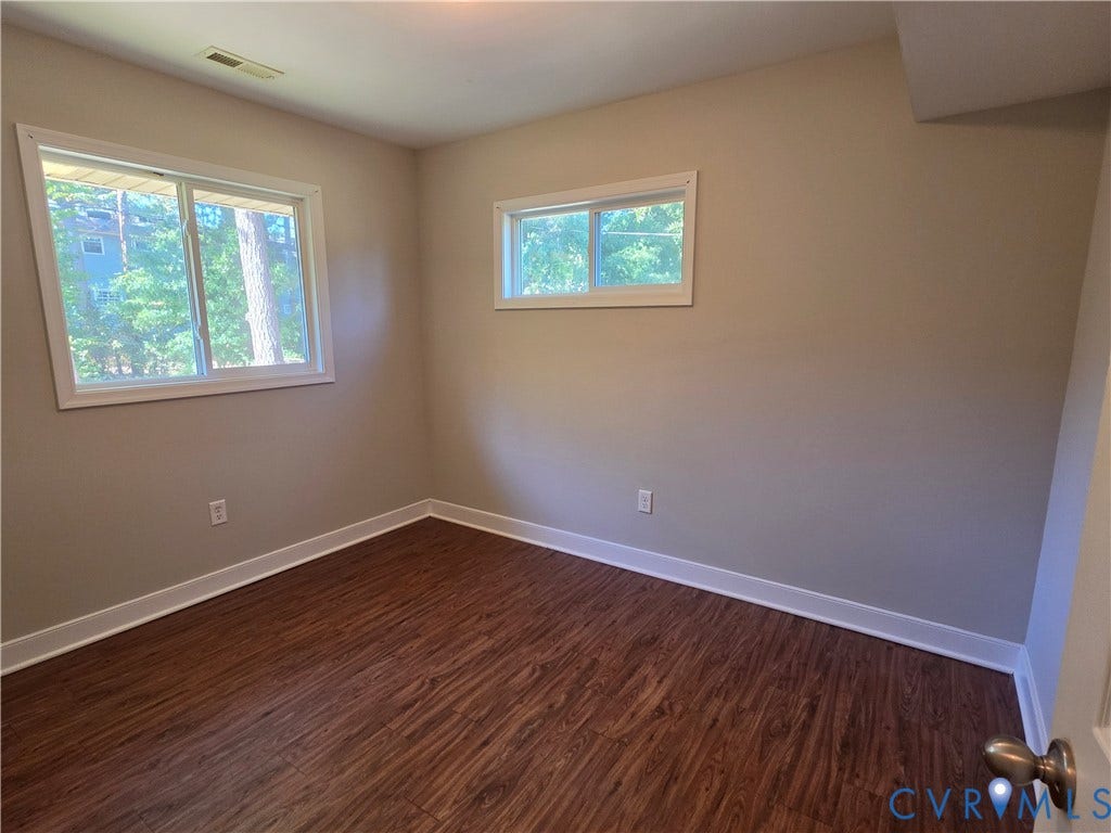 Wood-finish flooring with white trim, two windows, and light neutral wall paint