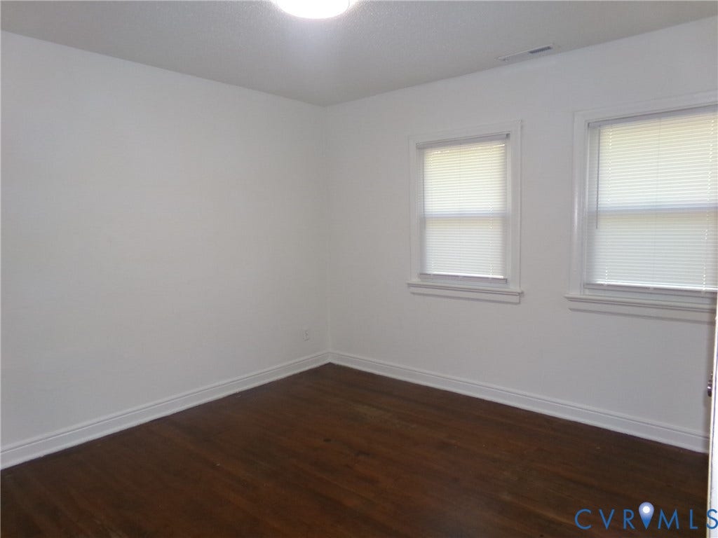 Hardwood-style flooring, white walls, two windows with blinds, and a ceiling-mounted light fixture