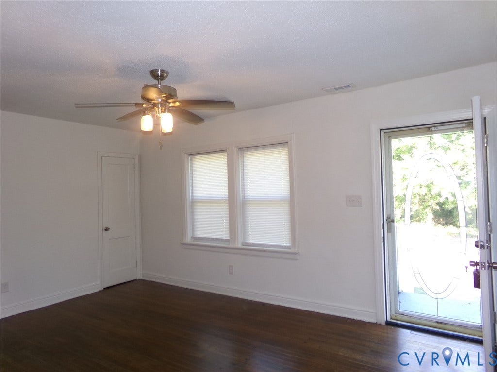 Wood-finish flooring, dual windows with blinds, ceiling fan with integrated lighting, white interior door, and a glass-paneled entry door
