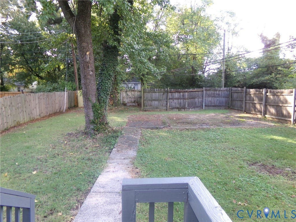 Expansive backyard featuring a manicured lawn, established mature trees, a concrete pathway, and a wood fence