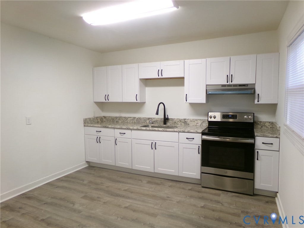 Kitchen featuring white shaker cabinetry, light-toned countertops, wood-finish flooring, stainless steel range, and a black gooseneck faucet