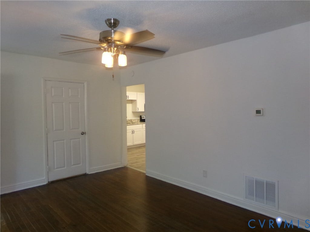Spacious room featuring dark wood-finish flooring, ceiling fan with integrated lighting, white six-panel closet door, and neutral wall finishes