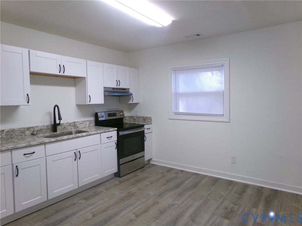 White cabinetry with dark hardware, granite-style countertops, stainless steel appliances, a stainless steel sink with a dark-finish faucet, and wood-finish flooring
