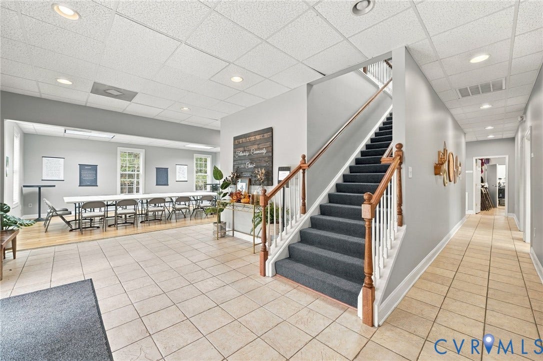 Neutral tile flooring throughout, carpeted staircase with wood handrails, recessed lighting, and a spacious room with hardwood flooring