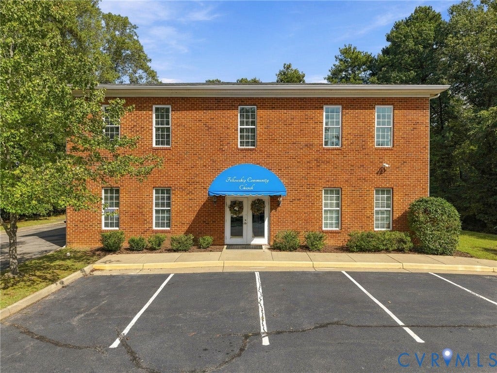 Two-story brick exterior with multiple windows, a blue entrance awning, and dedicated parking