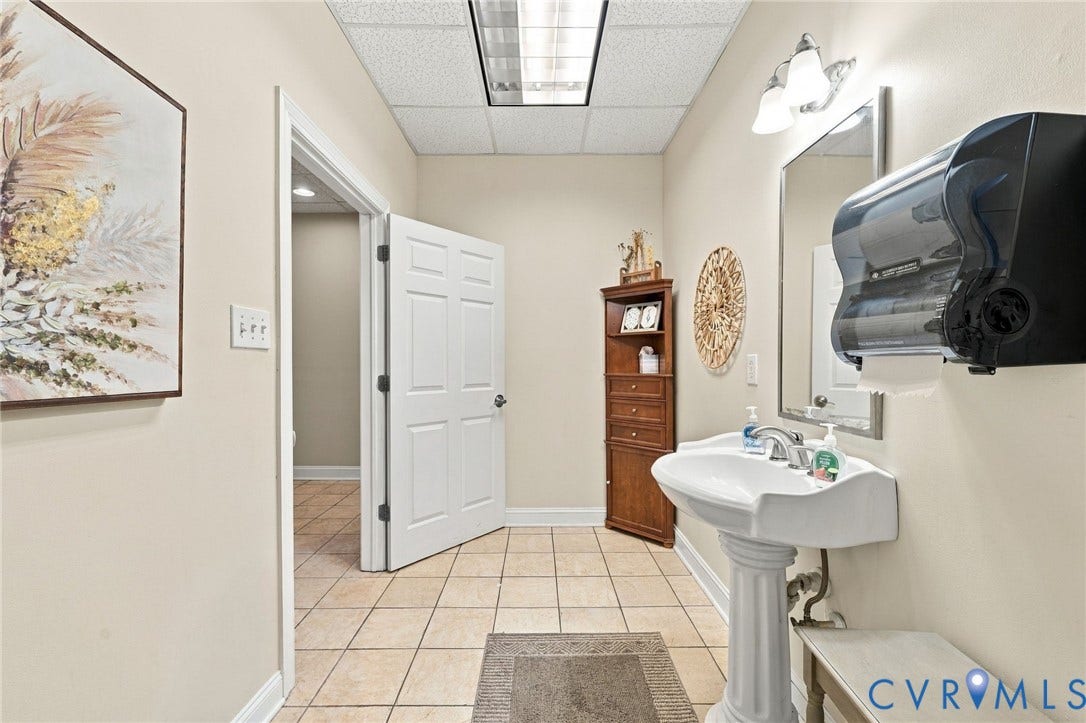 Pedestal sink with chrome fixtures, wall-mounted mirror, and tile flooring