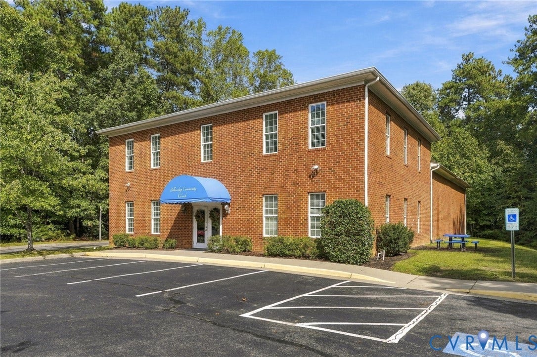 Brick-clad building featuring multiple window openings, a blue entrance awning, and an adjacent asphalt parking area