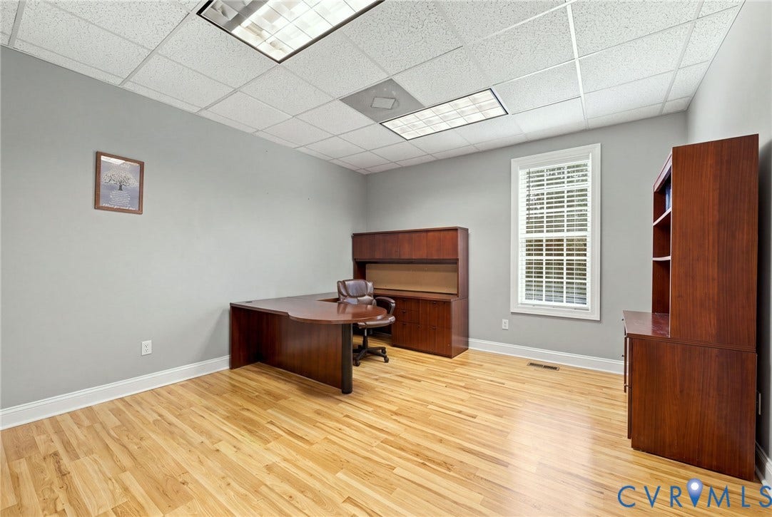 Hardwood-finish flooring, drop ceiling with integrated lighting, a single window with blinds, and light gray wall paint