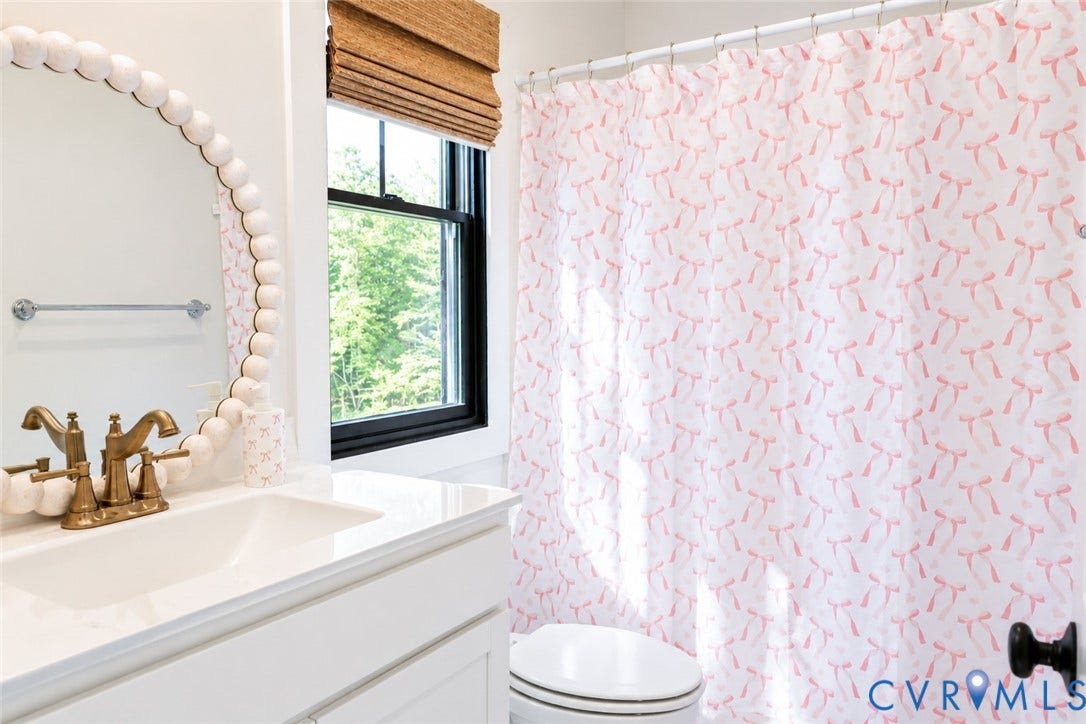 6265 Bushnell Drive, Rochambeau Estates, New Kent, VA 23124 Built-in vanity with a white countertop and undermount sink, antique brass finish faucet, and an oval mirror with a beaded frame