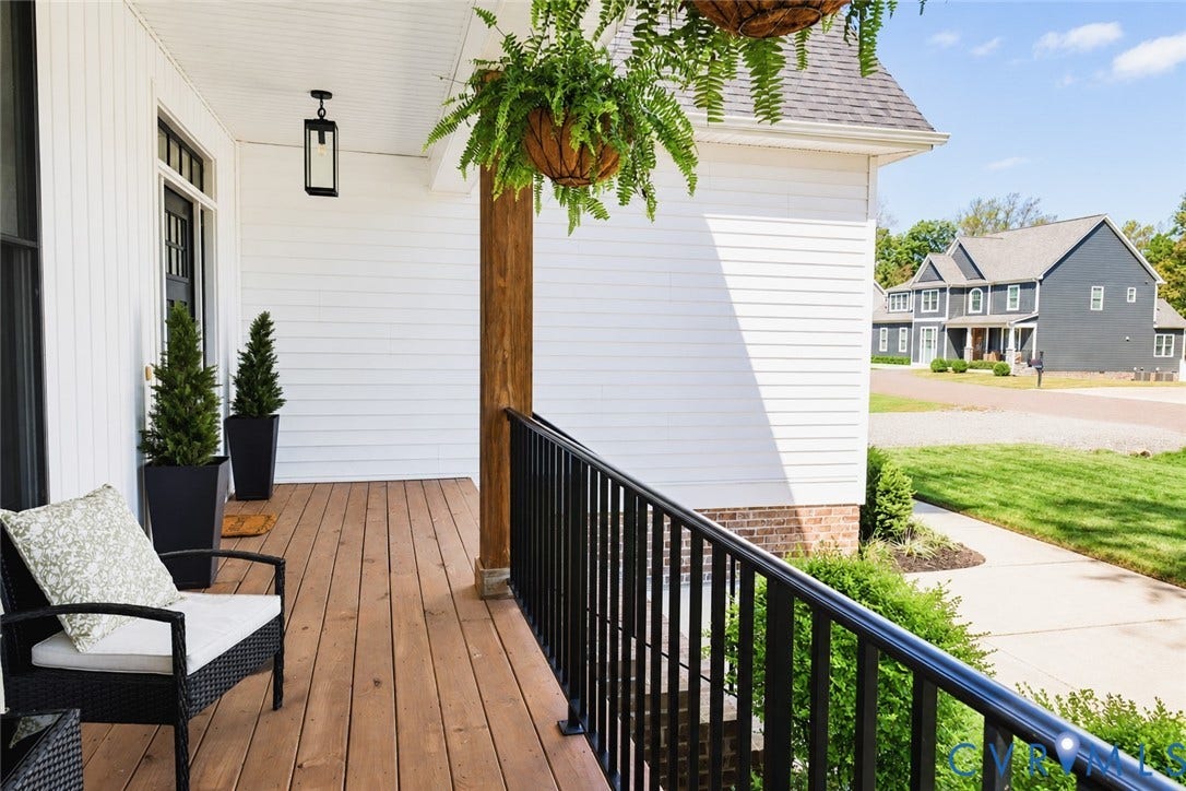6265 Bushnell Drive, Rochambeau Estates, New Kent, VA 23124 Expansive front porch featuring wood-finish decking, white horizontal siding, a substantial wood post, and a black metal railing