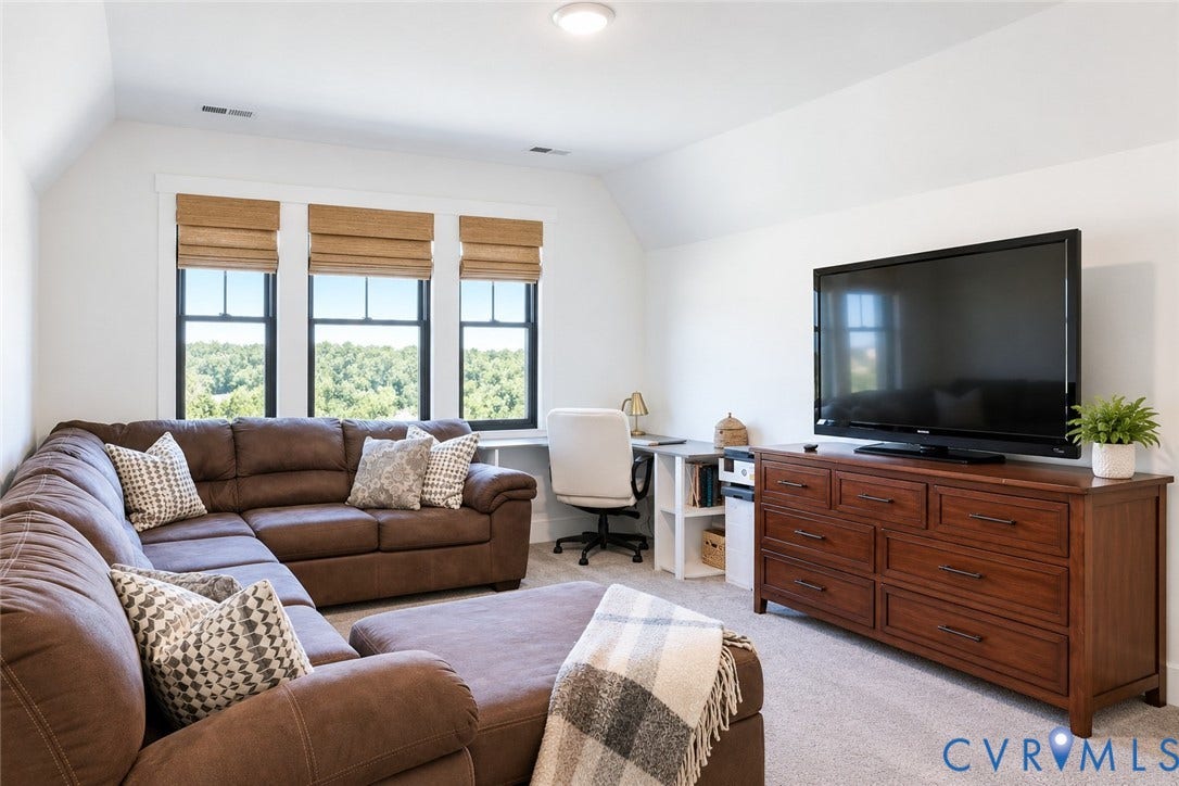 6265 Bushnell Drive, Rochambeau Estates, New Kent, VA 23124 Recessed lighting illuminates a spacious room featuring carpeting and multiple windows with woven Roman shades