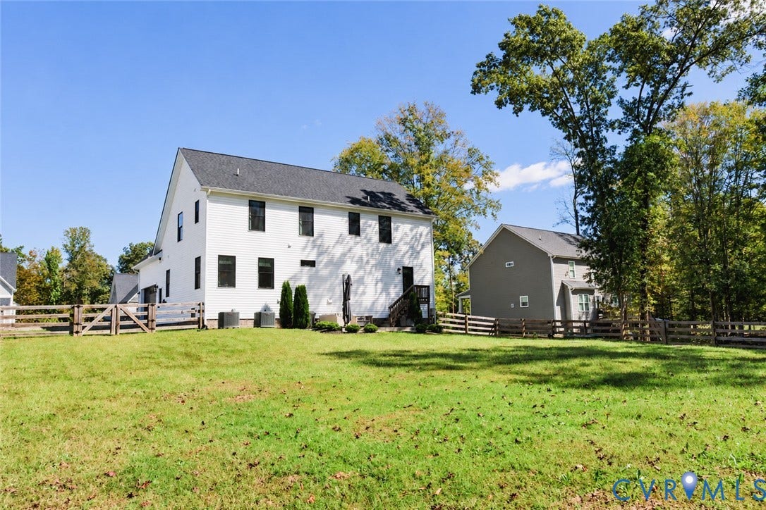 6265 Bushnell Drive, Rochambeau Estates, New Kent, VA 23124 Expansive green space with a split-rail fence, mature trees, and a two-story white exterior with a dark roof