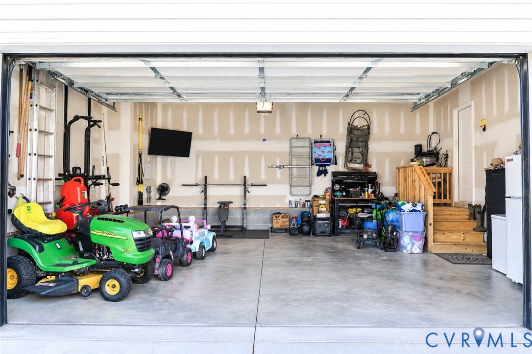 6265 Bushnell Drive, Rochambeau Estates, New Kent, VA 23124 Interior garage space featuring a concrete floor, light-toned walls, and a wooden staircase