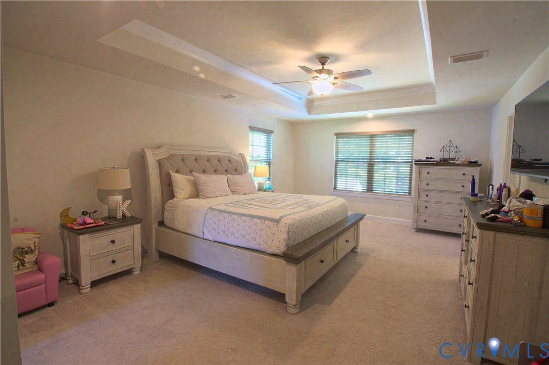 Recessed ceiling with integrated lighting, ceiling fan, two windows with blinds, and wall-to-wall carpeting