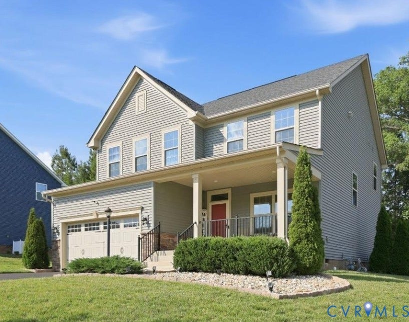 Two-story residence featuring light-colored siding, an integrated front porch with columns, a two-car garage, and landscaped front yard with shrubs and decorative stone