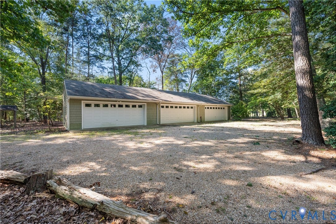Detached garage structure with three individual garage doors, horizontal siding, and a gravel surface
