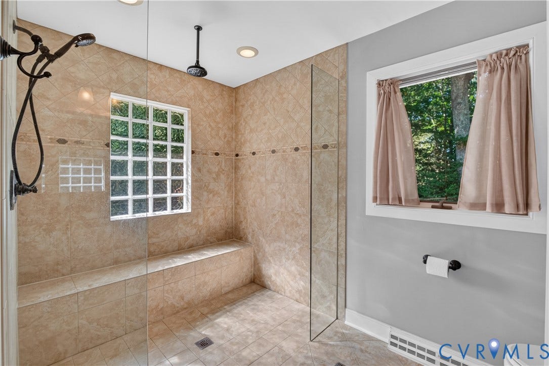 Walk-in shower with tiled walls and flooring, integrated bench, glass block window, and dual shower heads