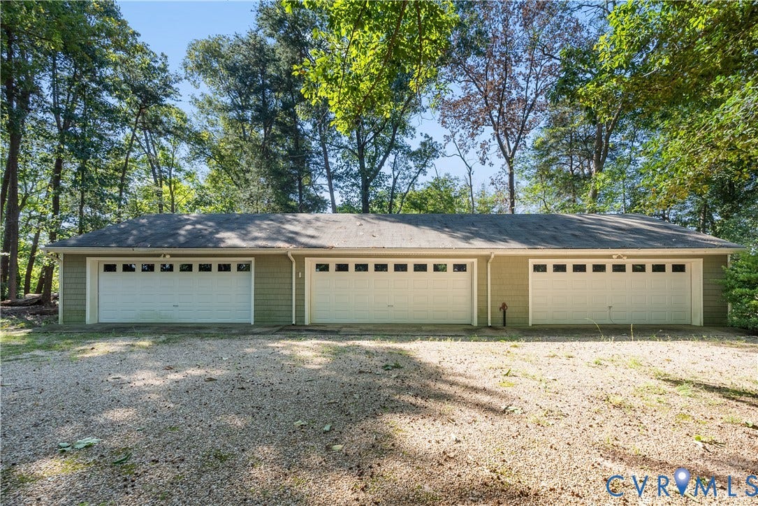 Three garage doors with window accents, horizontal siding in a neutral tone, and a gravel driveway