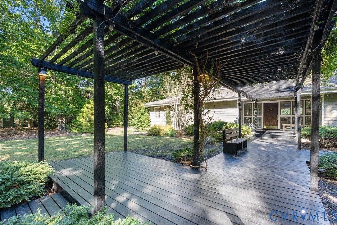 Expansive exterior wood deck with an attached pergola featuring built-in lighting and lush surrounding greenery