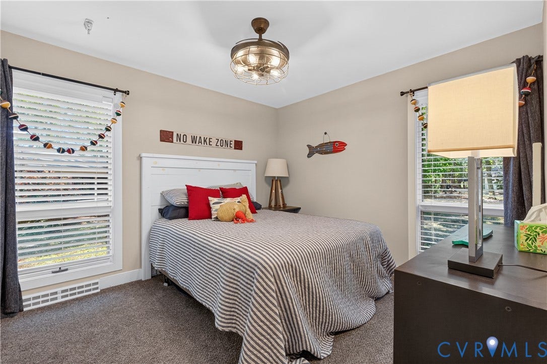 Recessed lighting, ceiling fan with integrated lighting, two windows with horizontal blinds, carpeted flooring, and a white paneled headboard