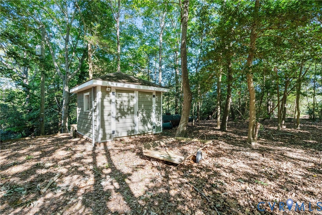 Detached storage shed with horizontal siding and a window, surrounded by mature trees
