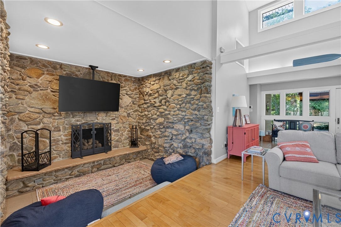 Stone-clad fireplace with a hearth, wood-finish flooring, recessed lighting, and high ceilings with clerestory windows