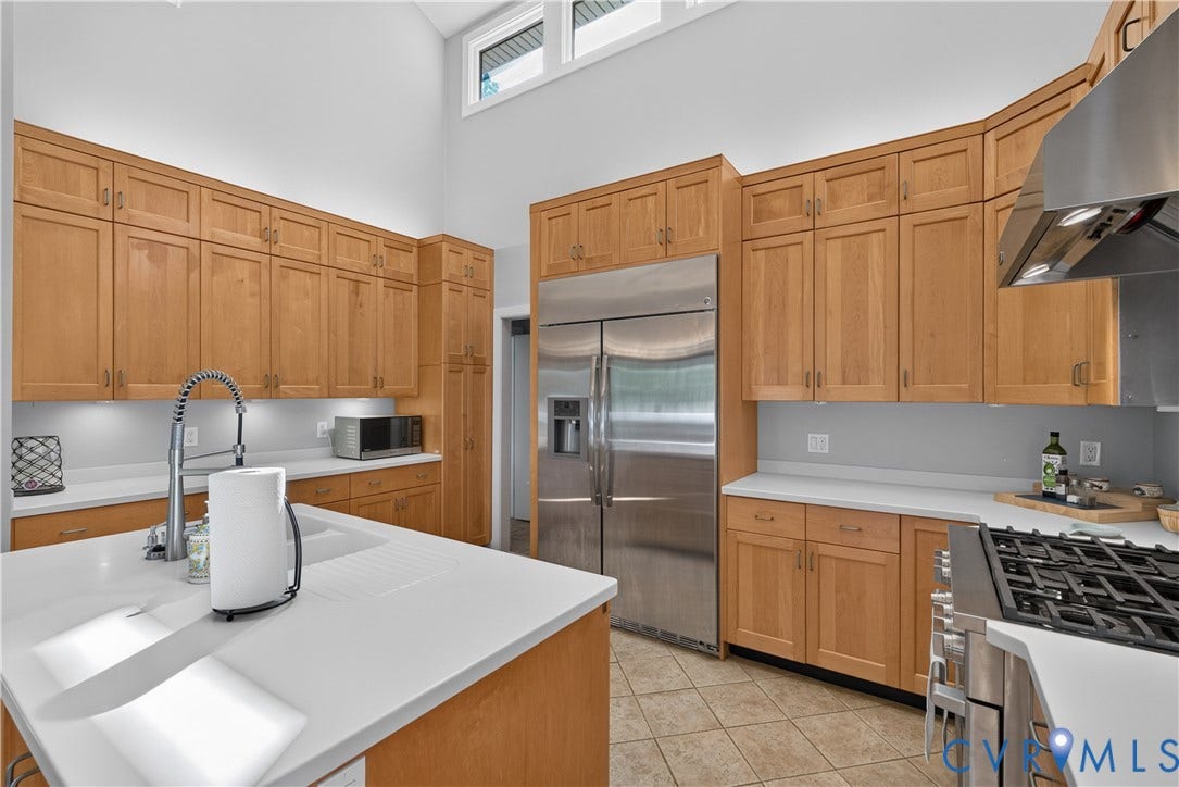 Vaulted ceiling with transom windows, recessed lighting, wood cabinetry, stainless steel appliances, and light-toned countertops