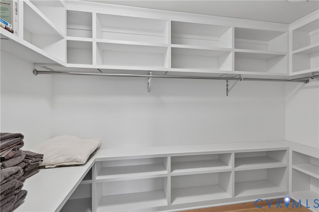 White built-in shelving, integrated hanging rods, and wood-finish flooring