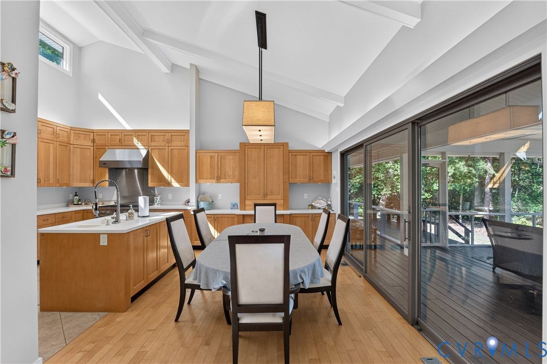 Vaulted ceilings with exposed beams, light wood-finish flooring, kitchen with light wood cabinetry, stainless steel range hood, and sliding glass doors to the exterior deck