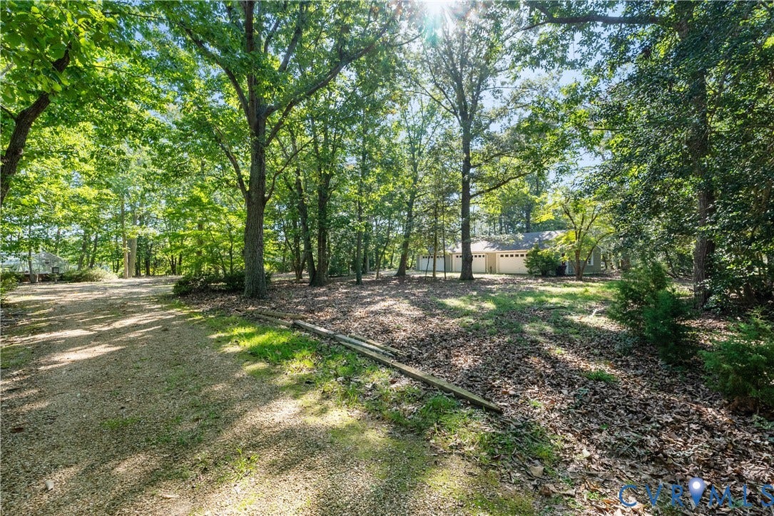 Gravel driveway leading to a residence with a multi-car garage, surrounded by a wooded landscape