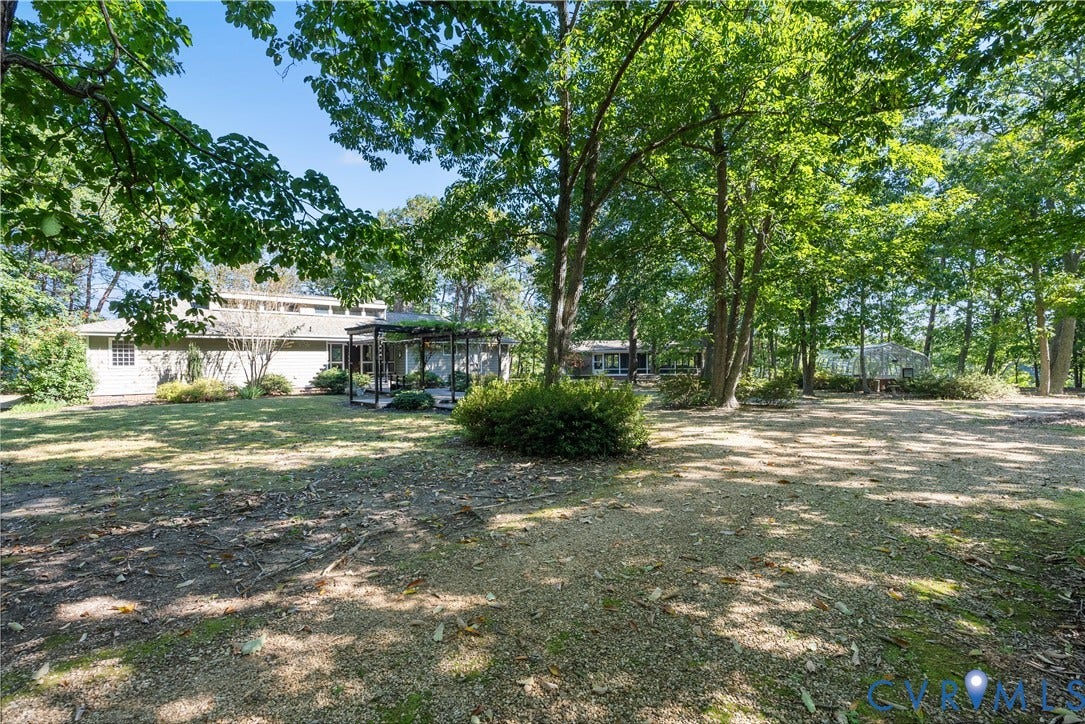 Expansive outdoor space featuring a pergola, mature trees, and a gravel-covered area