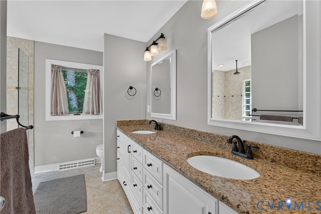 Dual vanity with granite countertops and integrated sinks, white cabinetry, dark bronze fixtures, and tile flooring