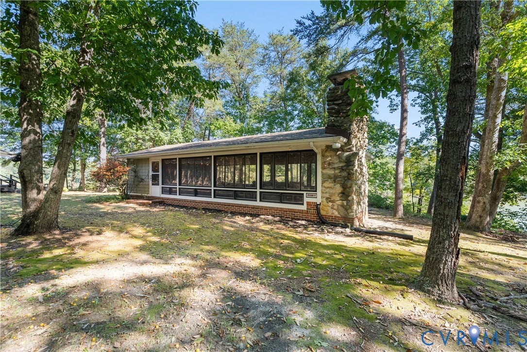 Screened porch with brick foundation, stone chimney, and surrounding mature trees