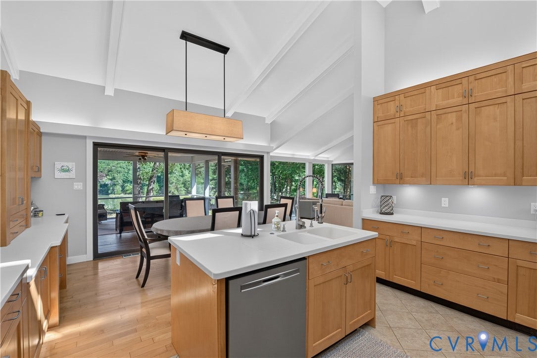 Kitchen featuring vaulted ceilings, light wood-finish cabinetry, white countertops, a central island with an integrated sink, and stainless steel appliances